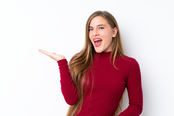 Teenager blonde girl over isolated white background holding copyspace imaginary on the palm to insert an ad