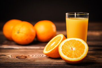Fresh orange juice in the glass cup with oranges on old wooden table.