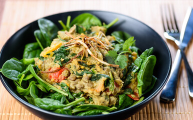 A serving of Vegetarian Dhal in a dark blue bowl, on a bamboo placemat and knife and fork to the side