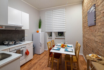 Modern contemporary interior of kitchen in loft apartment. Brick wall. Table and chairs. Fridge. White kicthen set.