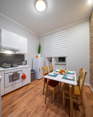 Modern contemporary interior of kitchen in loft apartment. Brick wall. Table and chairs. Fridge. White kicthen set.