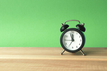 An alarm clock on a green background shows almost noon.