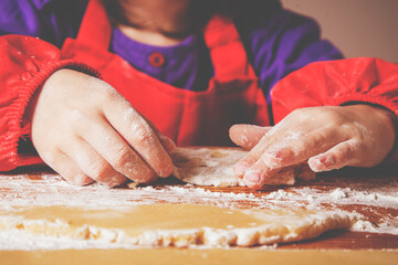 The concept of homemade pastry. Portrait of cute little child girl chef cooking cakes dough on wooden desk with flour.