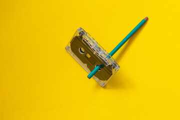 compact audio cassette and pencil on a yellow background