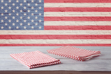 Empty wooden table with striped tablecloth over brick wall with american flag. 4th of july USA...