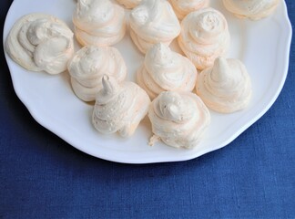 Obraz na płótnie Canvas Homemade french white meringues on a round plate, on a background of texture of blue linen cloth