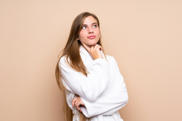 Fototapeta premium Teenager girl in a bathrobe over isolated background thinking an idea