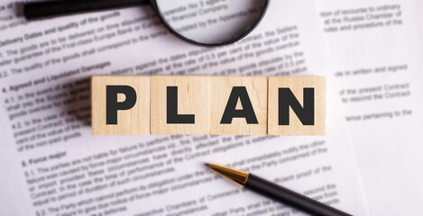 The word PLAN is written on wooden cubes that stand on the contract near the handle and magnifying glass