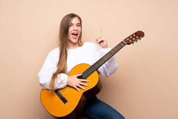 Teenager girl with guitar over isolated background pointing up a great idea