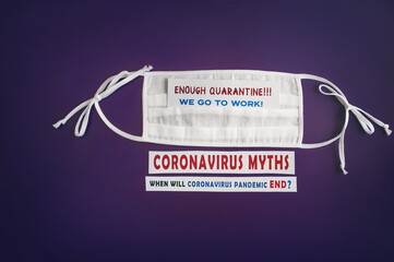 Medical mask on an isolated dark purple background with the inscription - Enough quarantine, we go to work. Coronavirus myths. When will coronavirus pandemic end. Stop coronavirus, COVID-19.