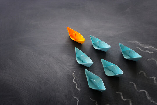 Leadership banner concept with paper boat on blackboard background. One leader ship leads others