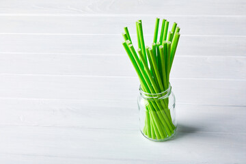 Green  environmentally friendly straws (biodegradable paper printed with soy-based ink) in a glass jar on white wooden background with copy space.