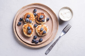 Healthy breakfast of cottage cheese pancakes, syrniki with blueberries and sour cream close-up in a plate on the table. light background