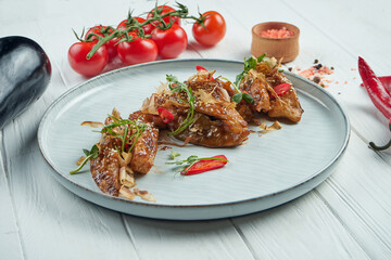 Asian-style fried eggplant in sweet and sour sauce with sesame seeds and hot chili peppers in a beautiful ceramic plate on a wooden background. Close up, selective focus