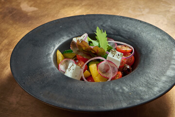 Classic greek salad with red onion, feta cheese, cucumber, bell pepper in a black plate on a copper, metal background. Close up view.