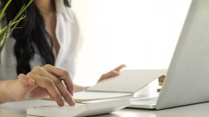 Close up of busineswosman or accountant hand holding pen working on calculator to calculate business data, accountancy document and laptop computer at office, business concept.