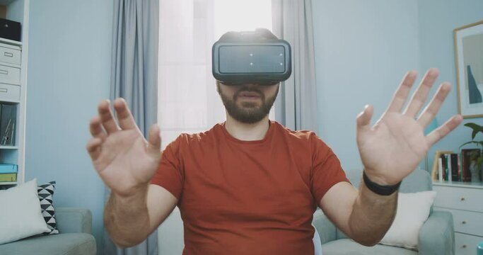 Close up of young man wearing virtual reality googles / VR Glasses in home office. Reading virtual online book, flipping pages, increasing and decreasing the size of objects. Concept of vr reality