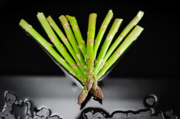 Fresh juicy asparagus laid out in the shape of an arrow on a black background in the water