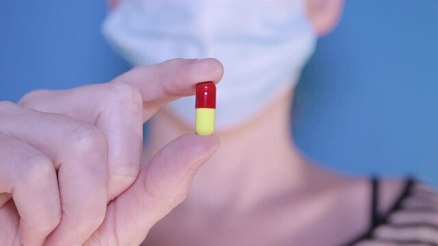 Person in a face mask holding up a medicine pill, closeup with a shallow depth of field 