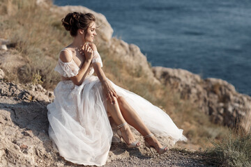 Beautiful bride stands on a cliff above the sea in a glamorous white wedding dress view of...