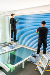 two male professional cleaners cleaning blue blinds on a large window front with micro fiber cloths