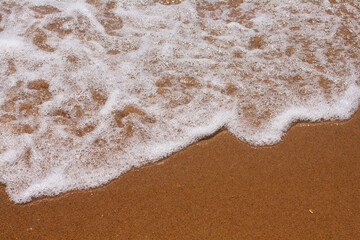 Foamy water comes to the sandy beach. The texture of the sandy beach