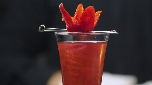 Close up ready made Strawberry Rossini Cocktail decorated with strawberry flower on a skewer. Glass is slowly rotating and moving on the slider