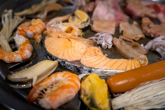 A Salmon sliced is grilling on the cha rcoal heat pan - Thai barbecue food. Selective focus at once part of salmon piece, photo contained noise due to low light environment.