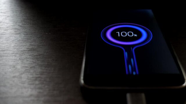 displaying 100 percent of the battery charge on the display of a mobile phone. mobile phone on a wooden table