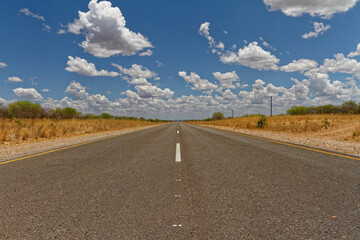 Center line desert road into the distant horizon with blue sky and white clouds