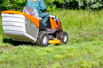 Fototapeta premium Green grass lawn and professional tractor lawnmower on a clear sunny day.