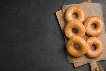 Delicious donuts on black table, top view. Space for text