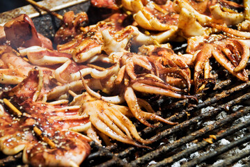 Stack of many grilled squid skewer on the grill in the night market.