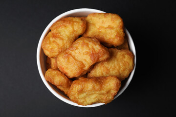 Bucket with delicious chicken nuggets on black background, top view
