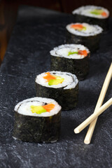 Japanese cuisine. Salmon sushi roll with avocado and cucumber on a dark stone plate. Close-up. Selective focus