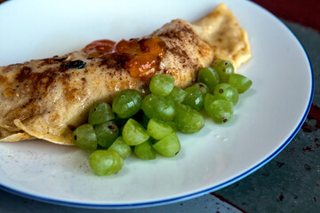 close-up of white plate with thin pancake and grapes