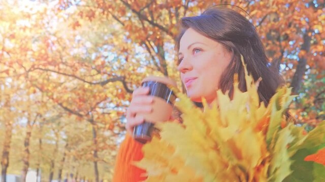 Happy smiling woman with autumn leaves drinking caffee in fall park,