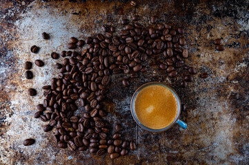Roasted coffee beans and cup of coffee on dark rusty background