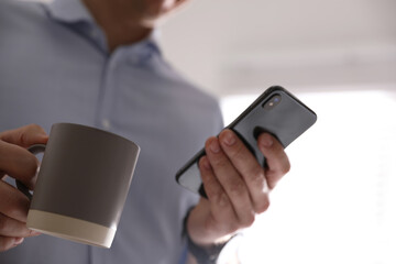 Man with cup and smartphone against light background, closeup of hands