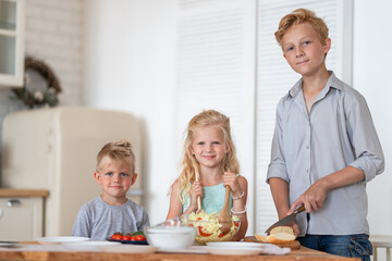 three blonde kids twoboys and girl on kitchen at home. Family eating healthy food , green salad on plates. Looking at camera.