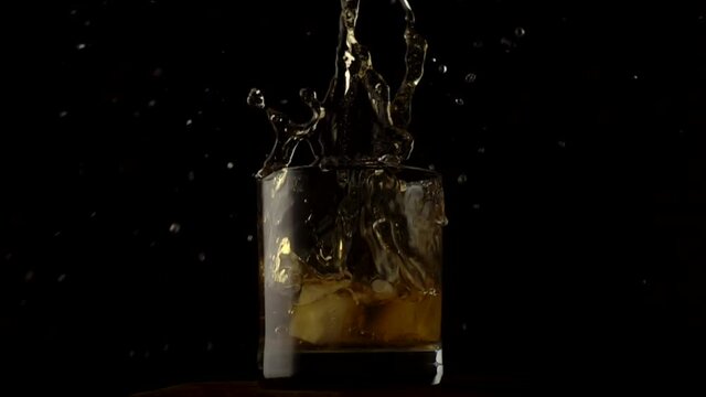 Ice cubes falling in glass with liquor, slow motion 500 fps