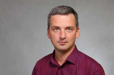 Portrait of a satisfied businessman in a red shirt on a gray background.