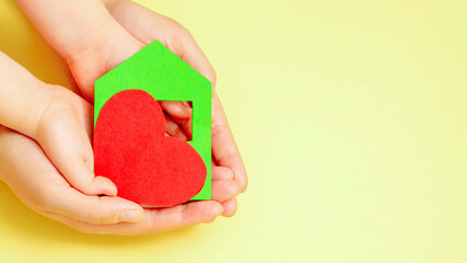 Paper house with heart in hands of child and dad on yellow background. Copy space.