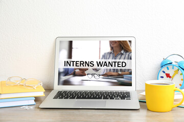 Modern laptop with text INTERNS WANTED on wooden table