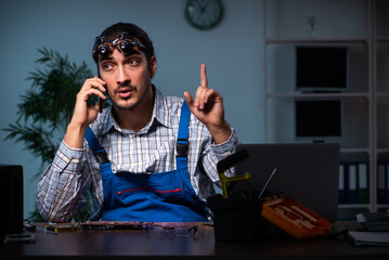 Young male technician repairing computer in workshop at night