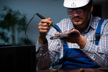 Young male technician repairing computer in workshop at night