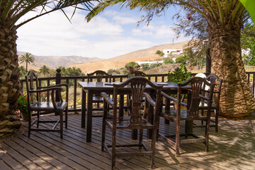 Blick von beschatteter Terrasse mit Tischen und Stühlen auf sonnige Wüstenlandschaft