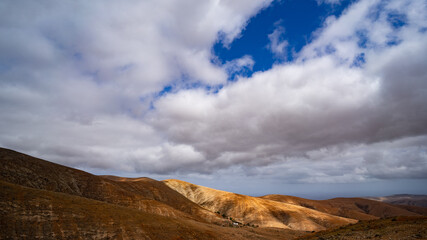 Sonne scheint golden durch Wolkenlöcher auf eine Hügelkette in wüstenartiger Landschaft