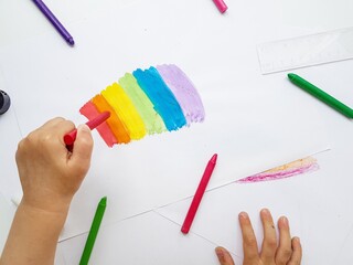 Colored wax crayons on white paper. A rainbow drawn by children's hands.