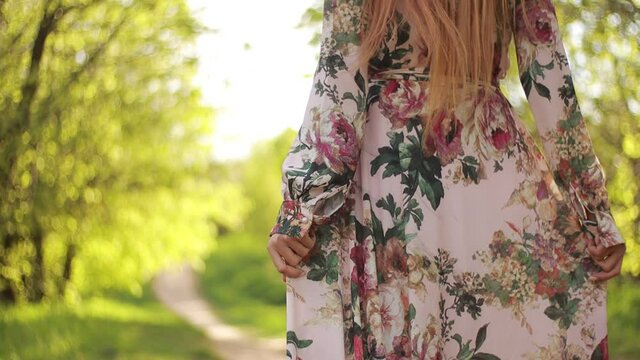 Video clip, blur effect and light fler, a young blonde woman with long hair in a long dress walks in a blossoming apple orchard on a sunny day in spring.